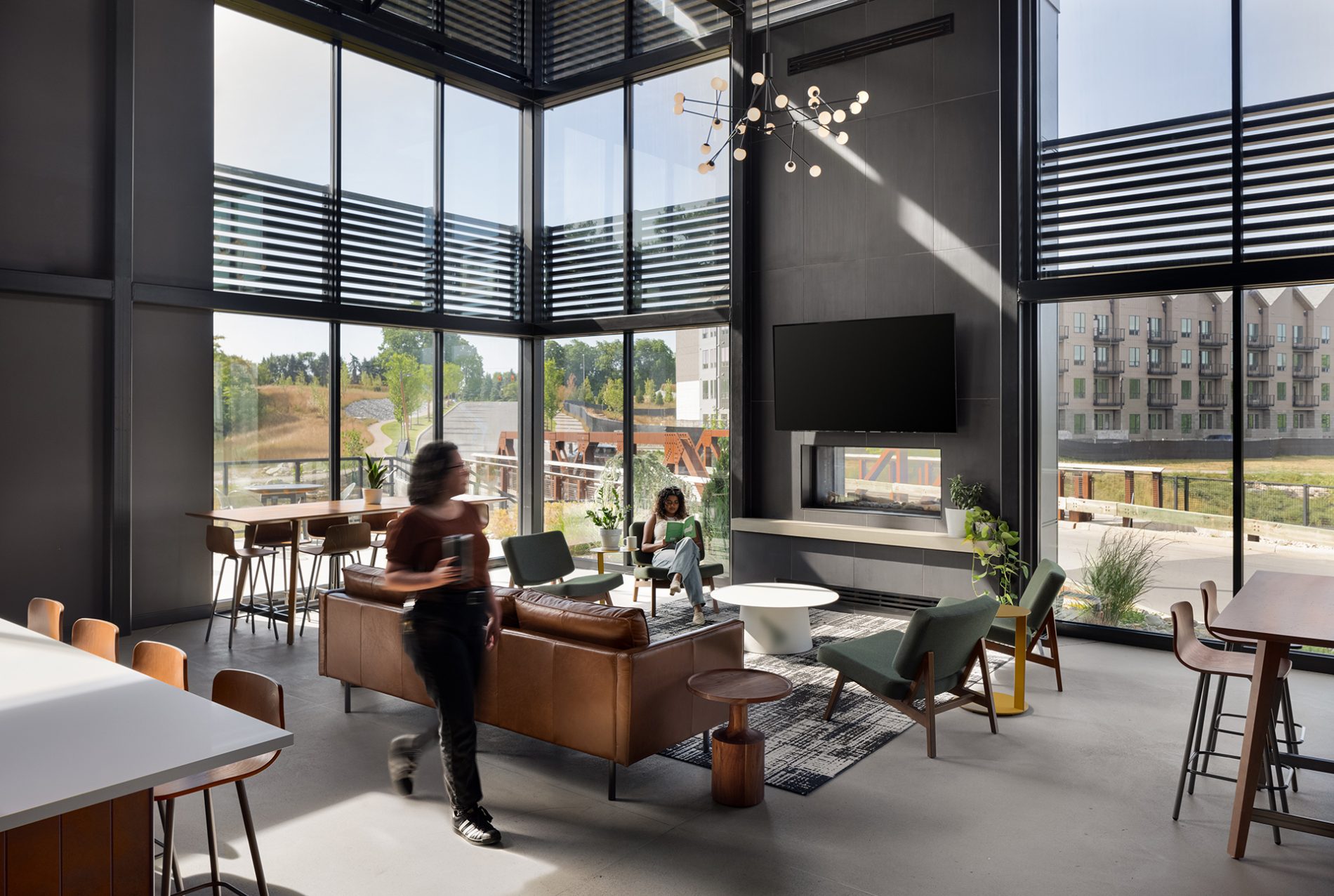 Interior of the Quarry Trails Clubhouse with modern furniture, fireplace, high ceilings, and 360 views through glass windows.