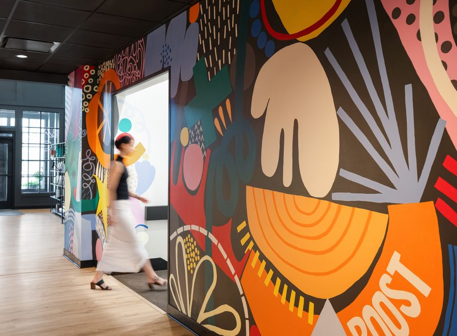 Penzone Base One hallway with a colorful and graphic mural created by Columbus-based artist Amy Haggard. A woman walks through the space to enter the downstairs storage area.